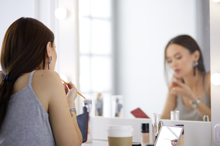 Young woman applying lipstick in front of a mirrorの写真素材