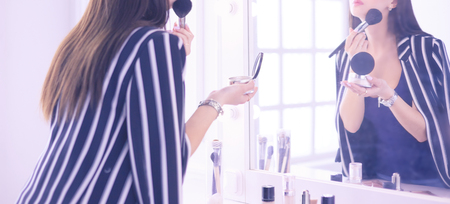 Beautiful girl looking in the mirror and applying cosmetic with a big brushの写真素材