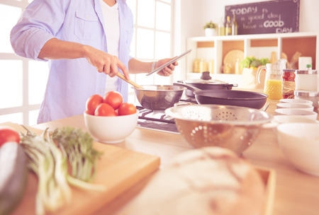 Man following recipe on digital tablet and cooking tasty and healthy food in kitchen at homeの写真素材