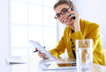 Businesswoman concentrating on work, using computer and cellphone in officeの写真素材