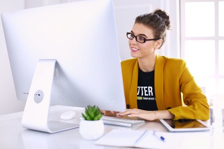 Young confident businesswoman working at office desk and typing with a laptop