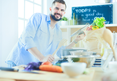Man following recipe on digital tablet and cooking tasty and healthy food in kitchen at homeの写真素材