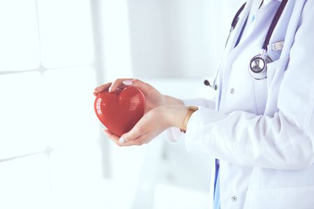 Female doctor with stethoscope holding heart, on light background.の写真素材