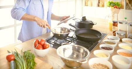 Man following recipe on digital tablet and cooking tasty and healthy food in kitchen at home.の写真素材