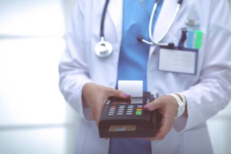 Doctor is holding payment terminal in hands. Paying for health care. Doctorの写真素材