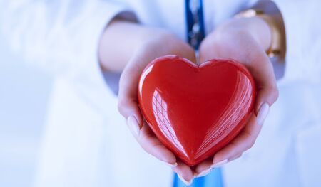 Female doctor with stethoscope holding heart, on light backgroundの写真素材