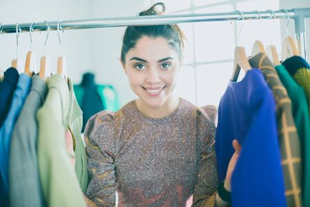 Beautiful young stylist near rack with hangersの写真素材