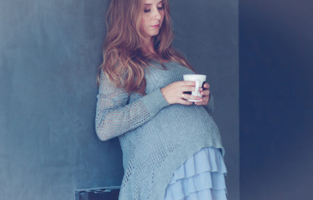 Pregnant woman with cup drinking tea looking through window at homeの写真素材