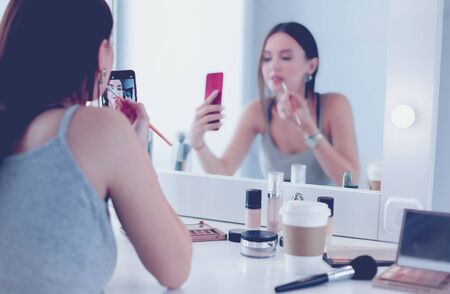Beauty blogger filming makeup tutorial with smartphone in front of mirrorの写真素材
