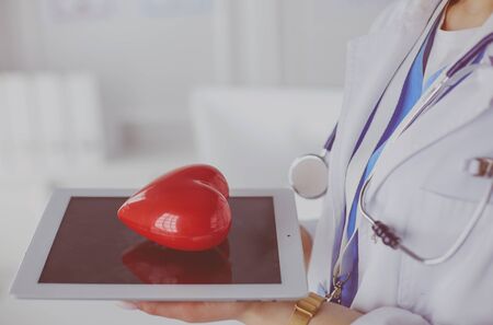 Female doctor with stethoscope holding heart, on light backgroundの写真素材