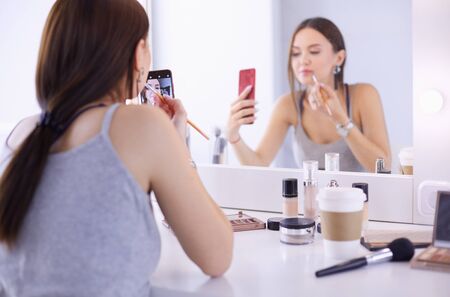 Beauty blogger filming makeup tutorial with smartphone in front of mirrorの写真素材