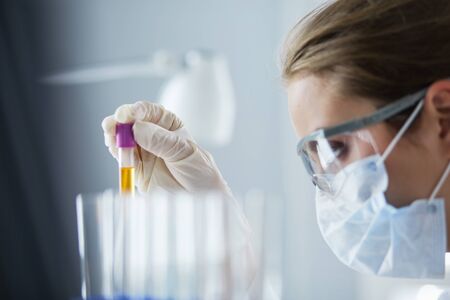 A medical or scientific researcher or doctor looking at a test tube of liquid green solution in a laboratoryの写真素材