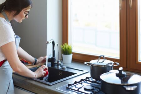 Woman washing vegetables. Beautiful young woman washing vegetables for salad and smiling while standing in the kitchen.の写真素材