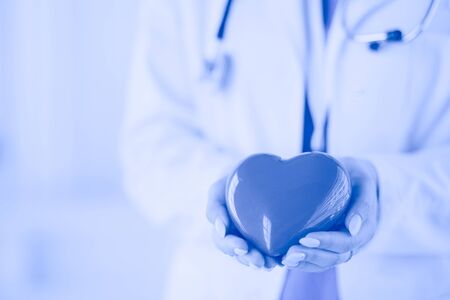Female doctor with stethoscope holding heart, on light background.の写真素材