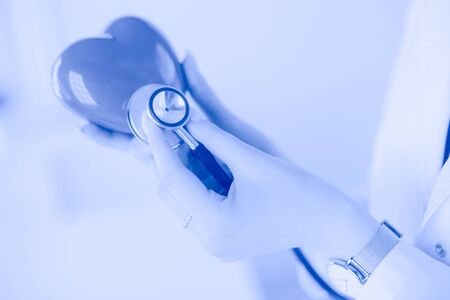A doctor with stethoscope examining red heart, isolated on white background.の写真素材