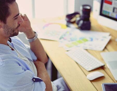 Portrait of young designer sitting at graphic studio in front of laptop and computer while working online.の写真素材