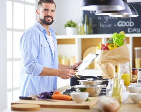 Man following recipe on digital tablet and cooking tasty and healthy food in kitchen at homeの写真素材