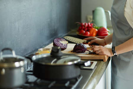 Young woman cutting vegetables in kitchen standing near desk.の写真素材