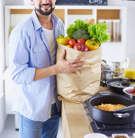 Man holding paper bag full of groceries on the kitchen background. Shopping and healthy food conceptの写真素材