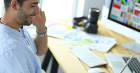 Portrait of young designer sitting at graphic studio in front of laptop and computer while working online.の写真素材
