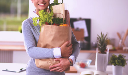 Young woman holding grocery shopping bag with vegetables Standing in the kitchen.