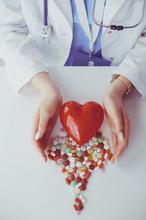Cardiologist with red heart and stethoscope at tableの写真素材