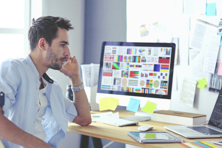 Portrait of young designer sitting at graphic studio in front of laptop and computer while working online.の写真素材