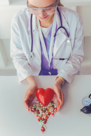 Cardiologist with red heart and stethoscope at tableの写真素材