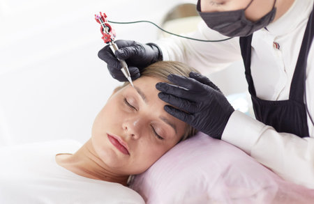 Young woman undergoing procedure of eyebrow permanent makeup in beauty salon