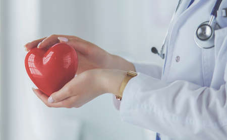 Female doctor with stethoscope holding heart, on light backgroundの写真素材