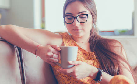 Young woman uses tablet while relaxing at home with coffee on the sofa couchの写真素材