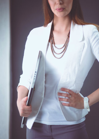 Young woman holding a laptop, standing on gray backgroundの写真素材