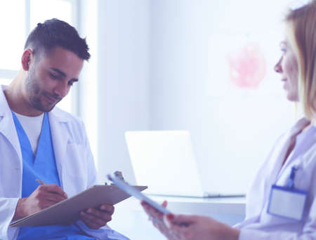 Handsome doctor is talking with young female doctor and making notes while sitting in his office.の写真素材