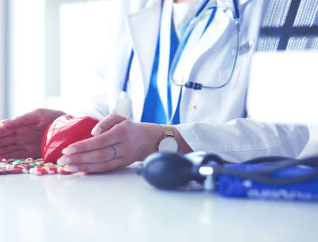 Cardiologist with red heart and stethoscope at tableの写真素材