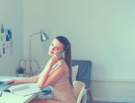 Young businesswoman sitting at the desk and talking on phoneの写真素材