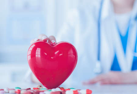 Doctor in white coat with stethoscope holding pills and plastic heart isolated on whiteの写真素材