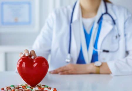 Doctor in white coat with stethoscope holding pills and plastic heart isolated on whiteの写真素材