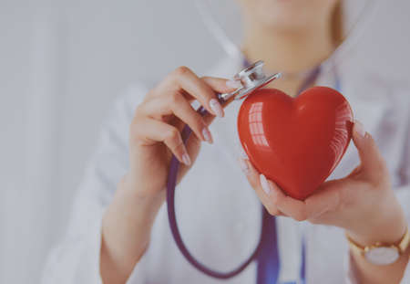 A doctor with stethoscope examining red heart, isolated on white backgroundの写真素材