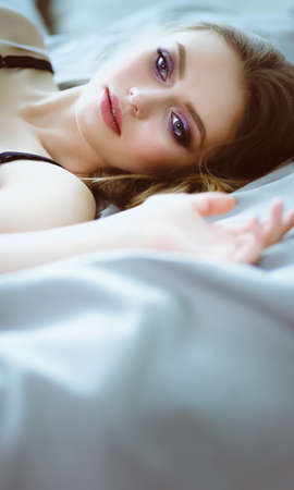 Beautiful young woman lying on white bedの写真素材