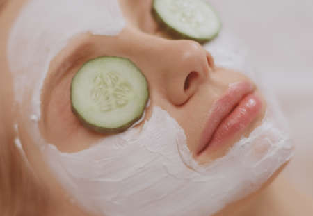 Beautiful young woman receiving facial mask of cucumber in beauty salonの写真素材