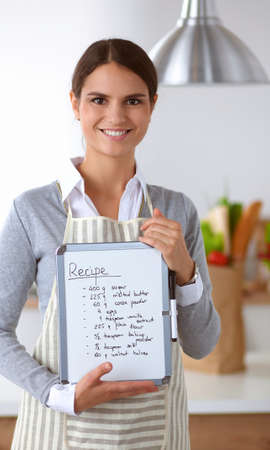Woman in the kitchen at home, standing near desk with folderの写真素材