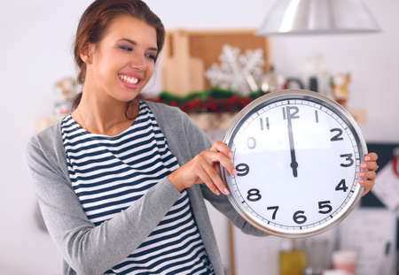 Happy young woman showing clock in christmas decorated kitchenの写真素材