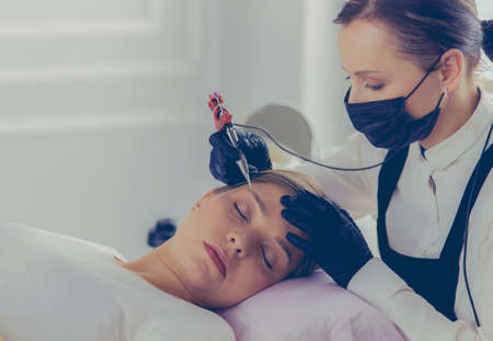 Young woman undergoing procedure of eyebrow permanent makeup in beauty salonの写真素材