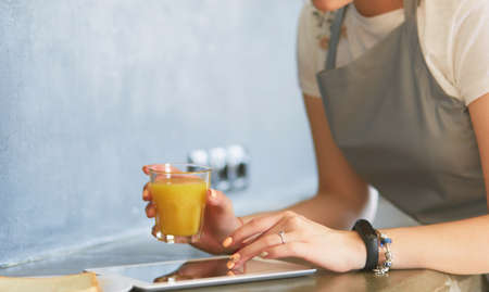 Young woman with orange juice and tablet in kitchenの写真素材