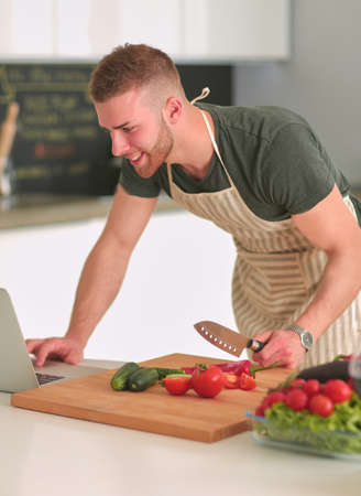 Portrait of man cooking vegetable in the kitchen while looking at a laptop computer on the tableの写真素材