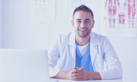 Portrait of a male doctor with laptop sitting at desk in medicalの写真素材