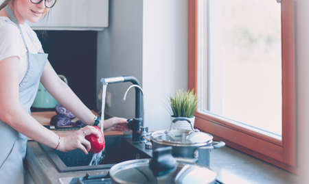Woman washing vegetables. Beautiful young woman washing vegetables for salad and smiling while standing in the kitchenの写真素材