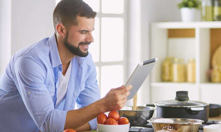 Man following recipe on digital tablet and cooking tasty and healthy food in kitchen at homeの写真素材