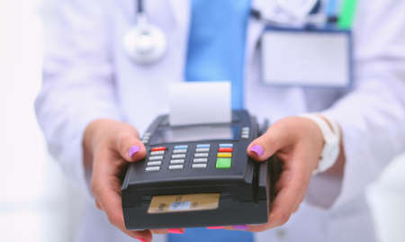 Doctor is holding payment terminal in hands. Paying for health care. Doctorの写真素材