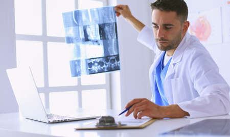 Handsome doctor is talking with young female patient and making notes while sitting in his office.の写真素材